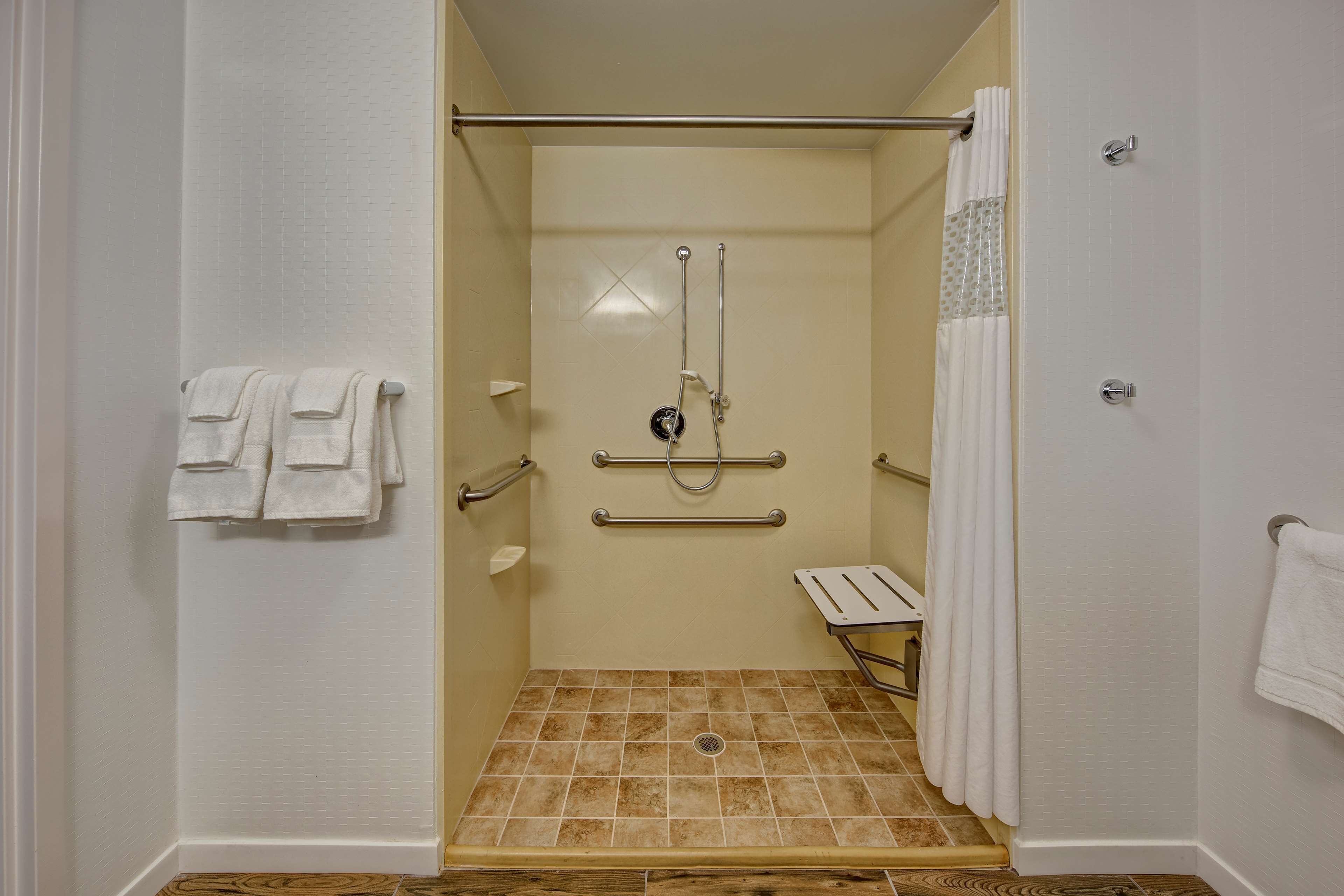 A handicap-accessible shower with grab bars, a bench, and a white towel rack.