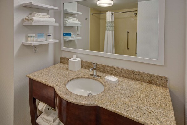 A bathroom with a granite countertop sink, a mirror, and shelves with towels and toiletries. - Hampton Inn by Hilton Dunn (Dunn)