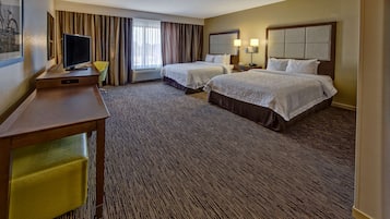 A hotel room with two beds, a desk, a television, and a chair.
