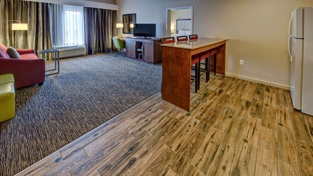 A hotel room with a wooden floor, a red sofa, a desk with a chair, a television, and a refrigerator. - Hampton Inn by Hilton Dunn (Dunn)
