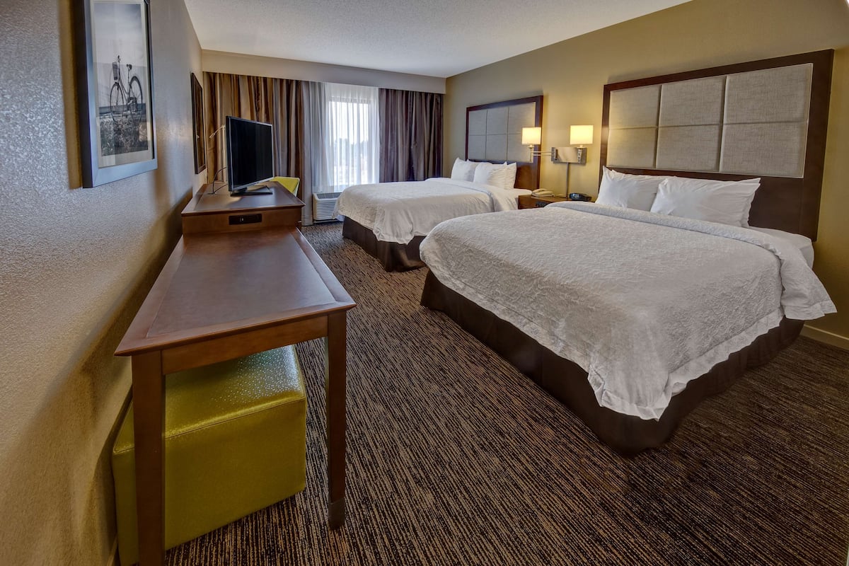 Quarto de hotel com duas camas, uma mesa, televisão e janela com cortinas.