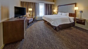 A hotel room with a large bed, a desk with a flat-screen TV, a chair, a bedside table with a lamp, and a window with curtains. - Hampton Inn by Hilton Dunn (Dunn)