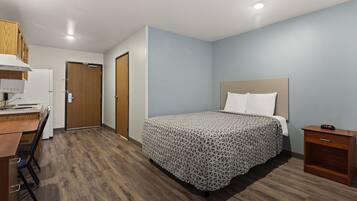 Una habitación de hotel con una cama, un escritorio con computadora, un armario de madera y una mesita de noche con un reloj.