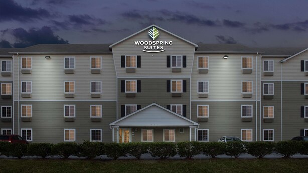 Een hotel met meerdere verdiepingen, een centrale ingang en een bord met daarop 'Woodspring Suites'.
