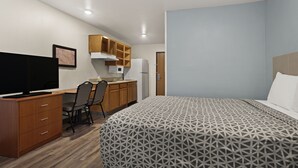 Een slaapkamer met een bed, een bureau met een computer, een stoel, een televisie en een kitchenette.