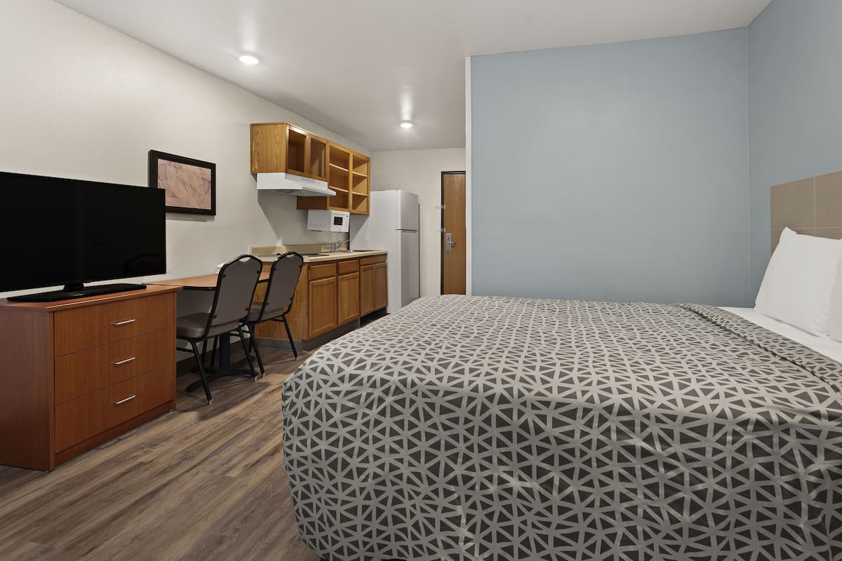 Une chambre comprenant un lit, un bureau avec un ordinateur, une chaise, un téléviseur et un coin cuisine.