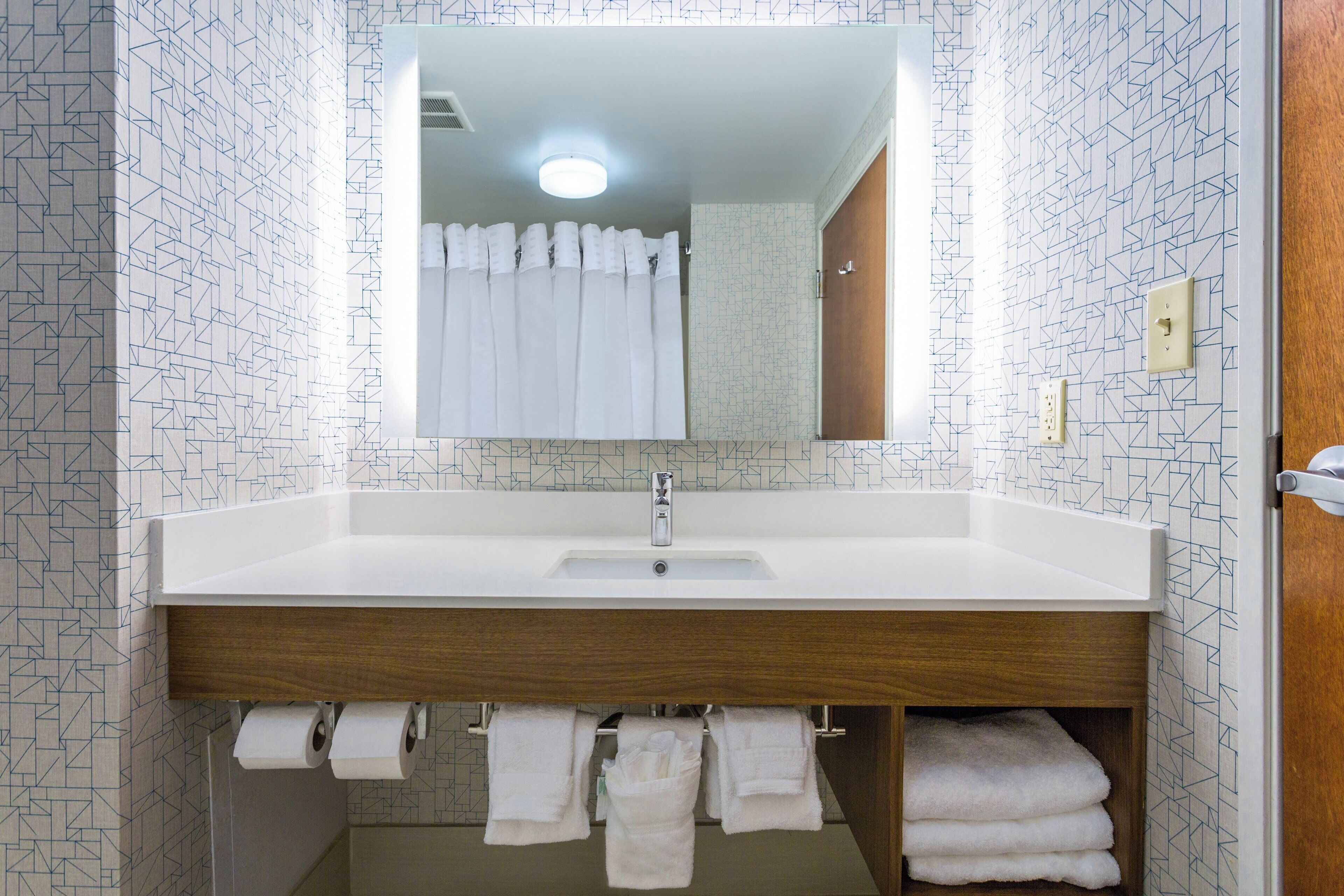 Une salle de bain avec un lavabo blanc, un miroir au-dessus et des carreaux muraux à motifs.