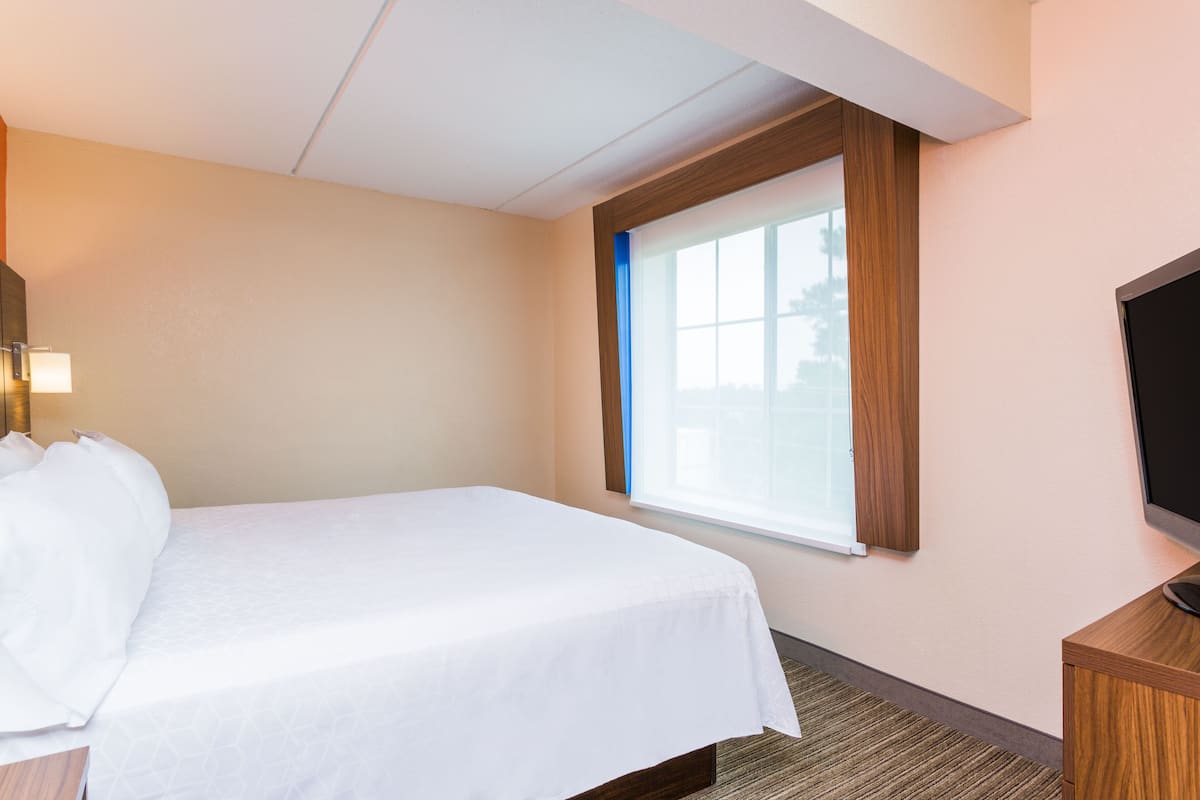 Une chambre d’hôtel avec un lit, une télévision et une fenêtre équipée de stores.