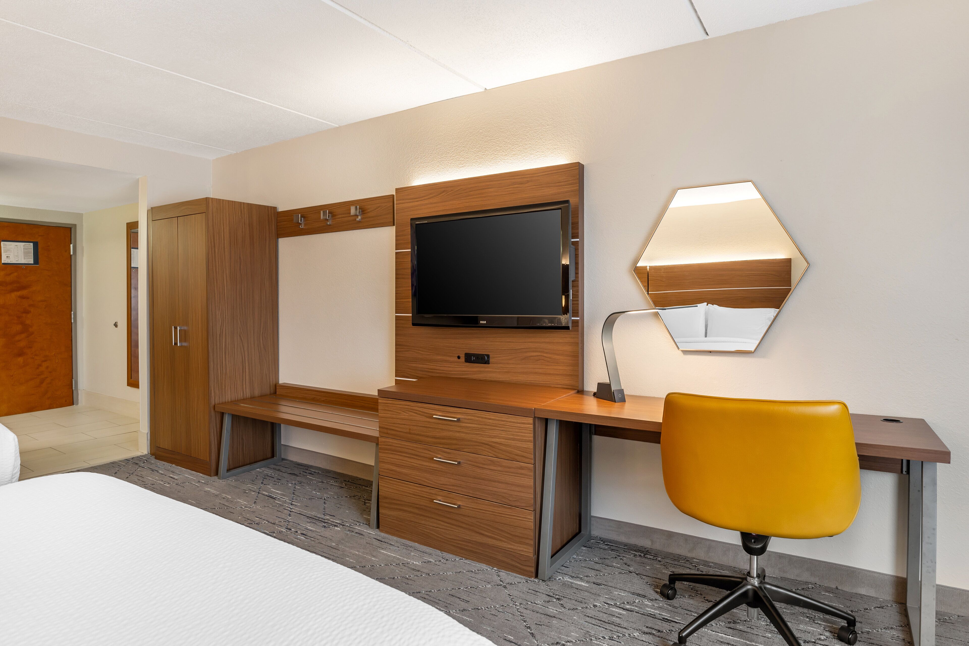 A hotel room with a bed, wooden desk, chair, TV, and wardrobe.