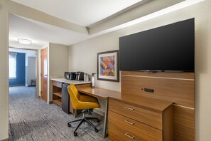 Hotelkamer met een houten bureau, een gele bureaustoel, een flatscreen televisie, een lijst met abstracte kunst en een kitchenette.