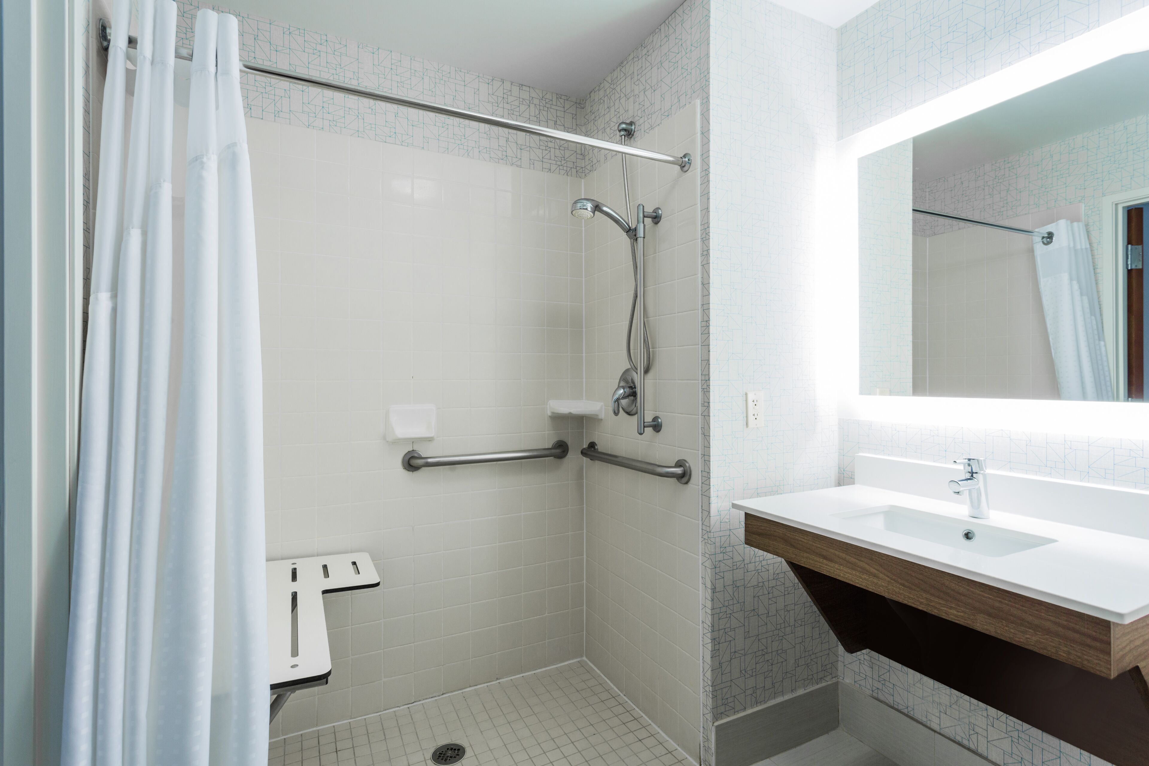 A bathroom with a shower, grab bars, a sink, and a mirror.