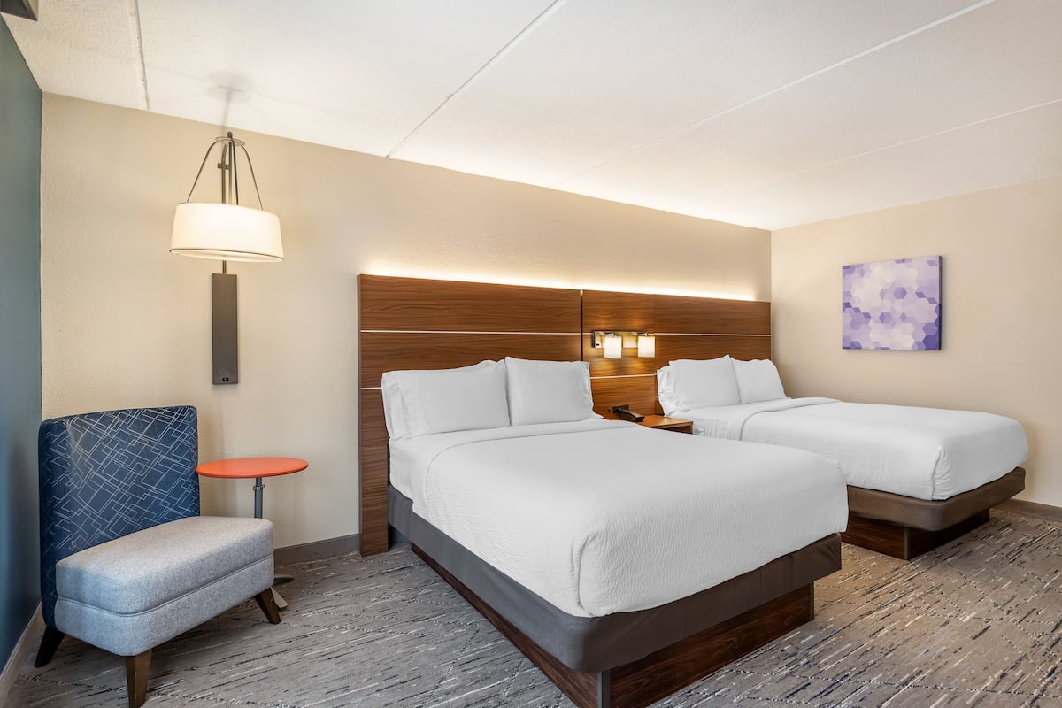 Une chambre d’hôtel avec deux lits, une petite table, une chaise et une lampe fixée au mur.