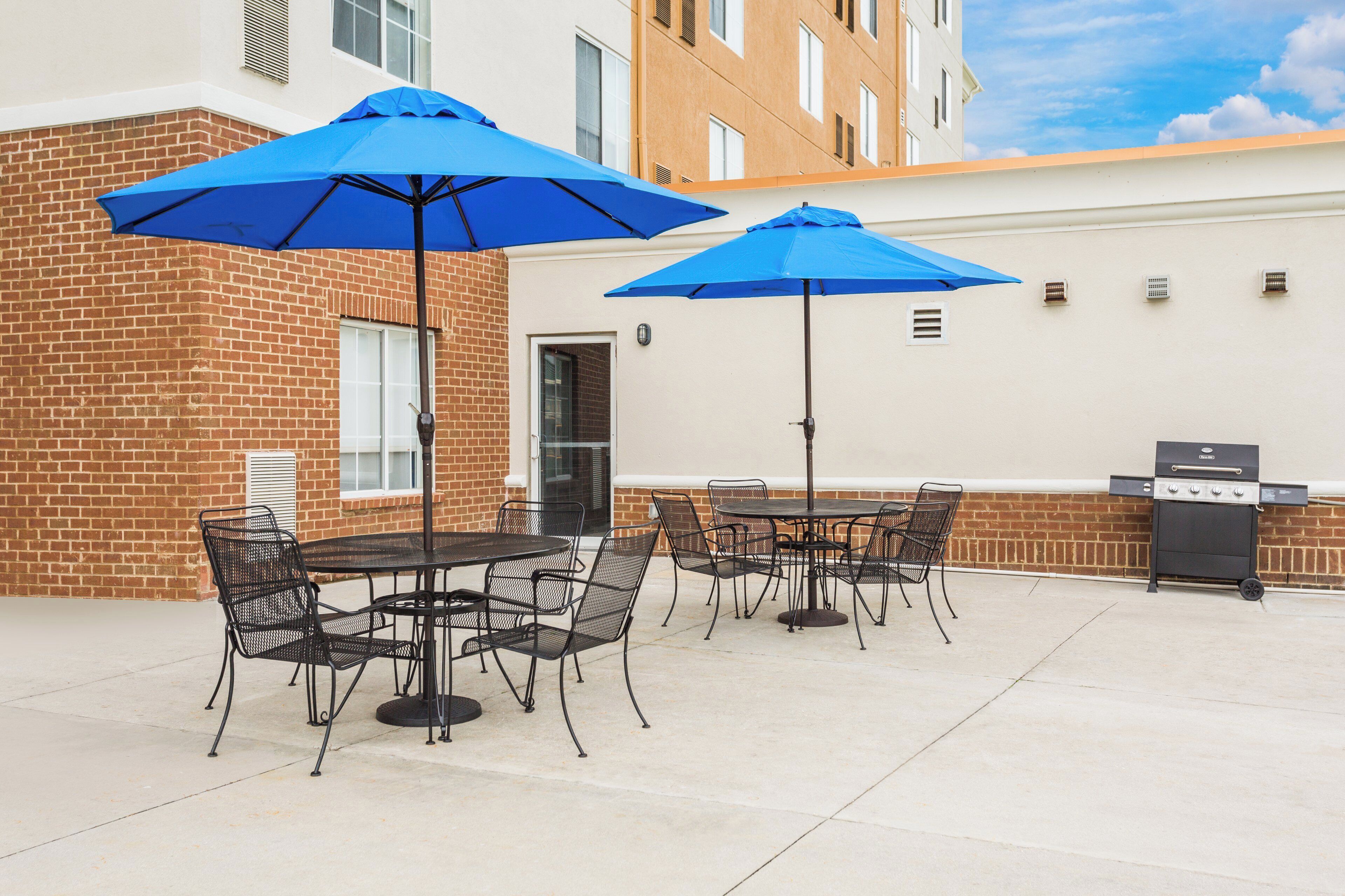 Une terrasse extérieure avec un mur en briques, un barbecue et une table avec des chaises.