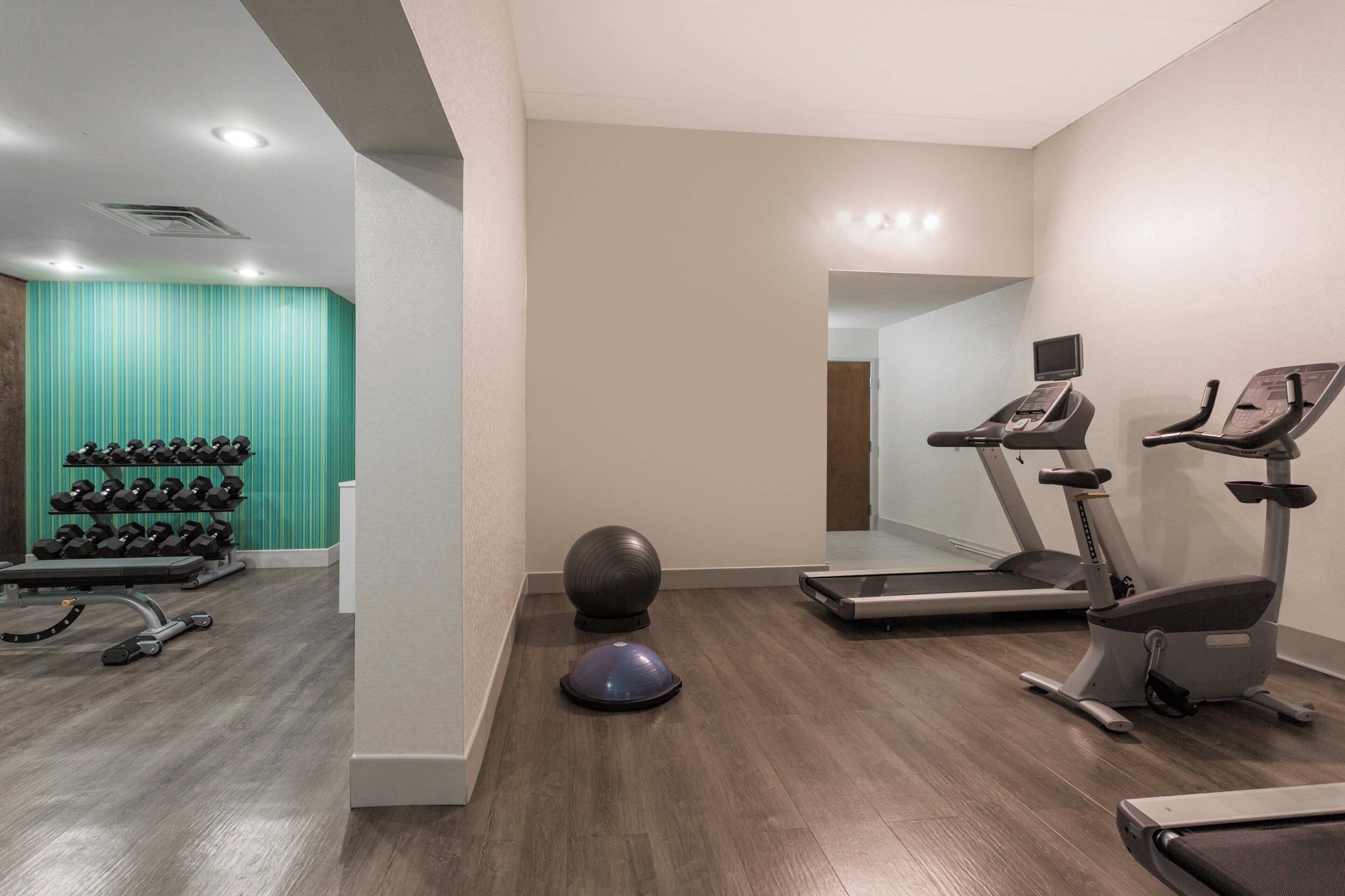A gym with exercise equipment, a mirrored wall, and a teal-striped wall.