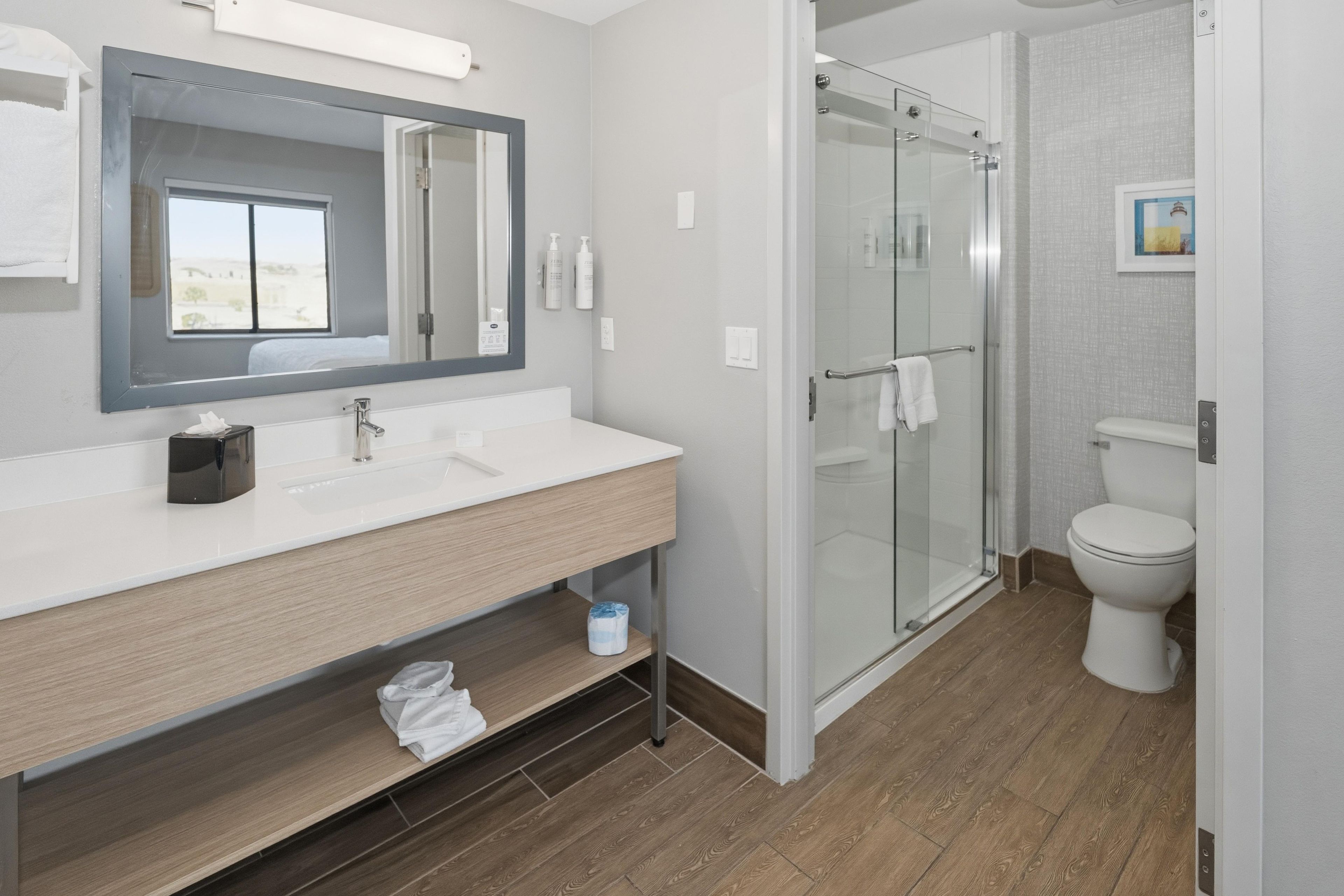 Un baño moderno con cabina de ducha de vidrio, inodoro blanco y tocador con espejo.