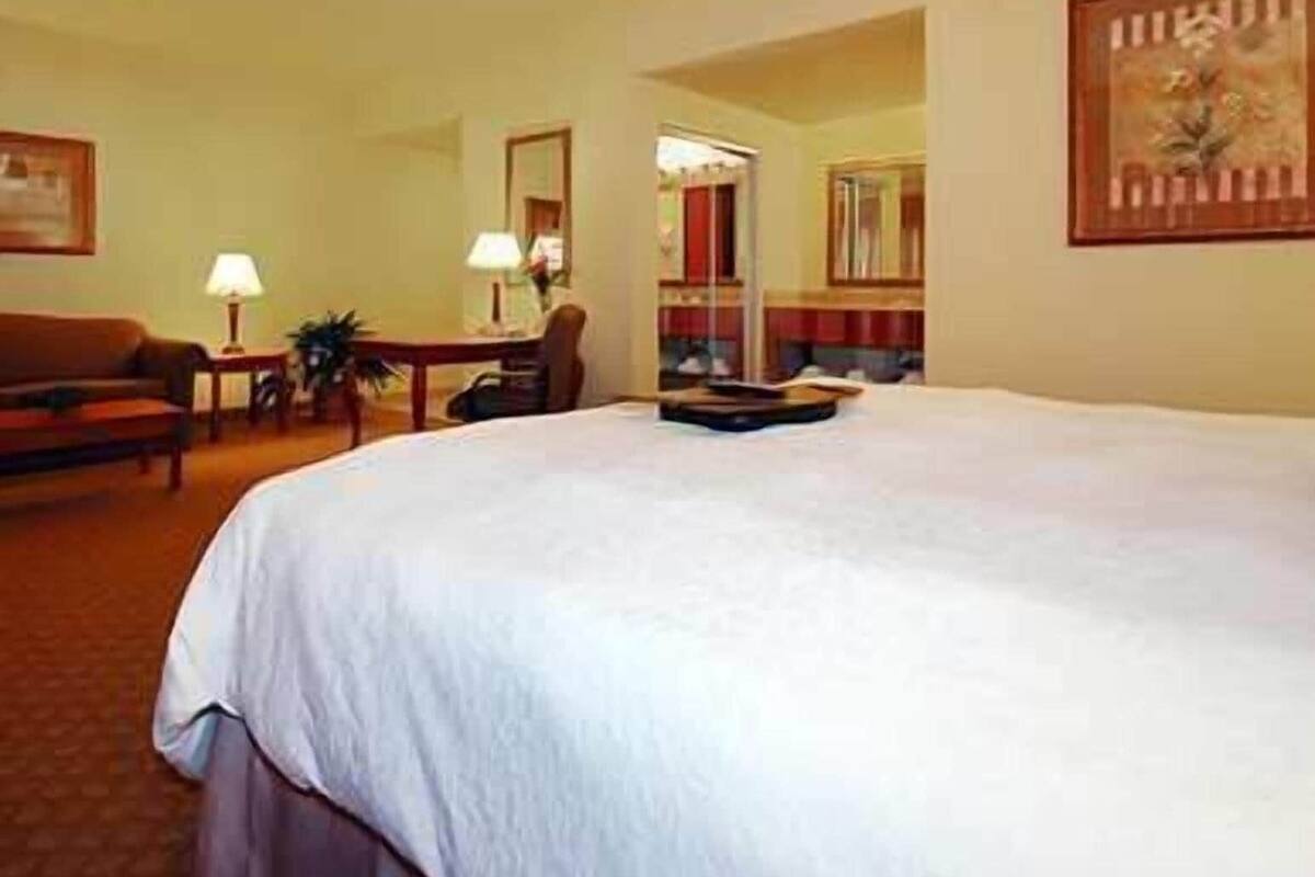 Una habitación de hotel con una cama grande, un escritorio, una silla, una lámpara y un cuadro en la pared.