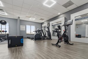 Un gimnasio con equipo de ejercicio, un espejo grande y un cartel con normas de acondicionamiento físico.