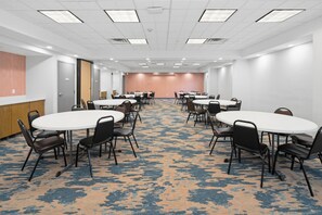 Un salón de conferencias con varias mesas y sillas, piso alfombrado y techo blanco con luces.