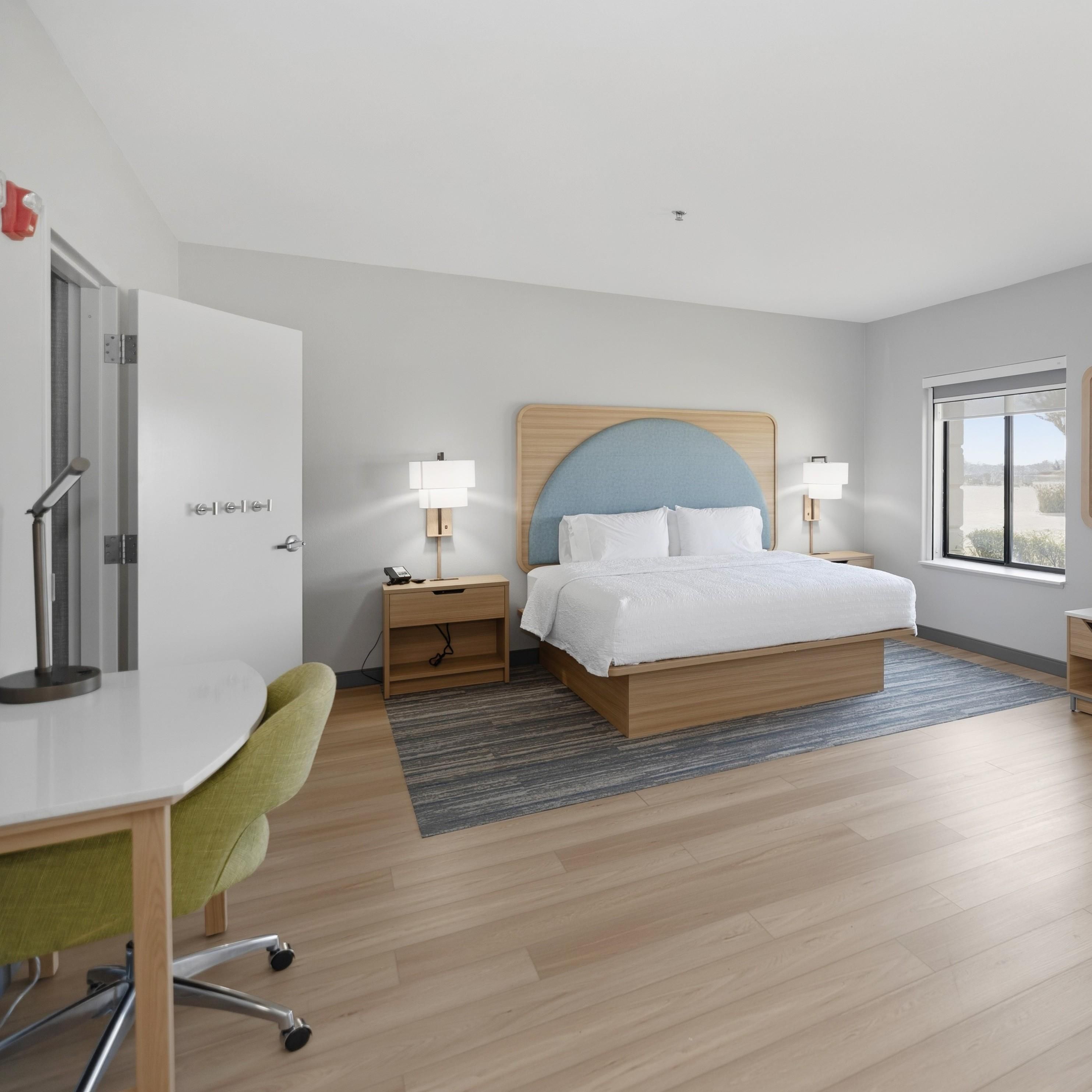 A modern hotel room with a bed, bedside tables, a desk, and a chair.
