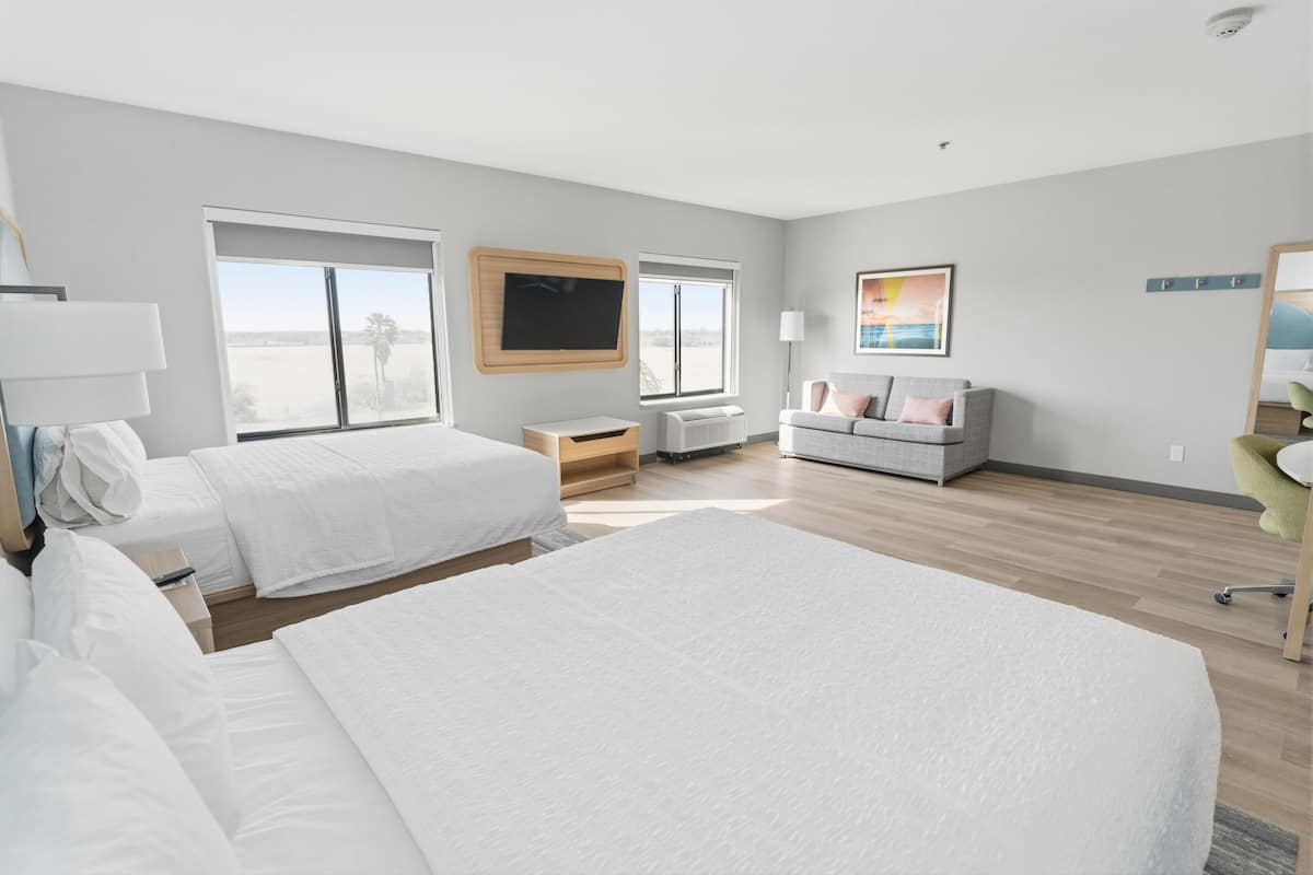A hotel room with two beds, a TV, a sofa, and a large window.