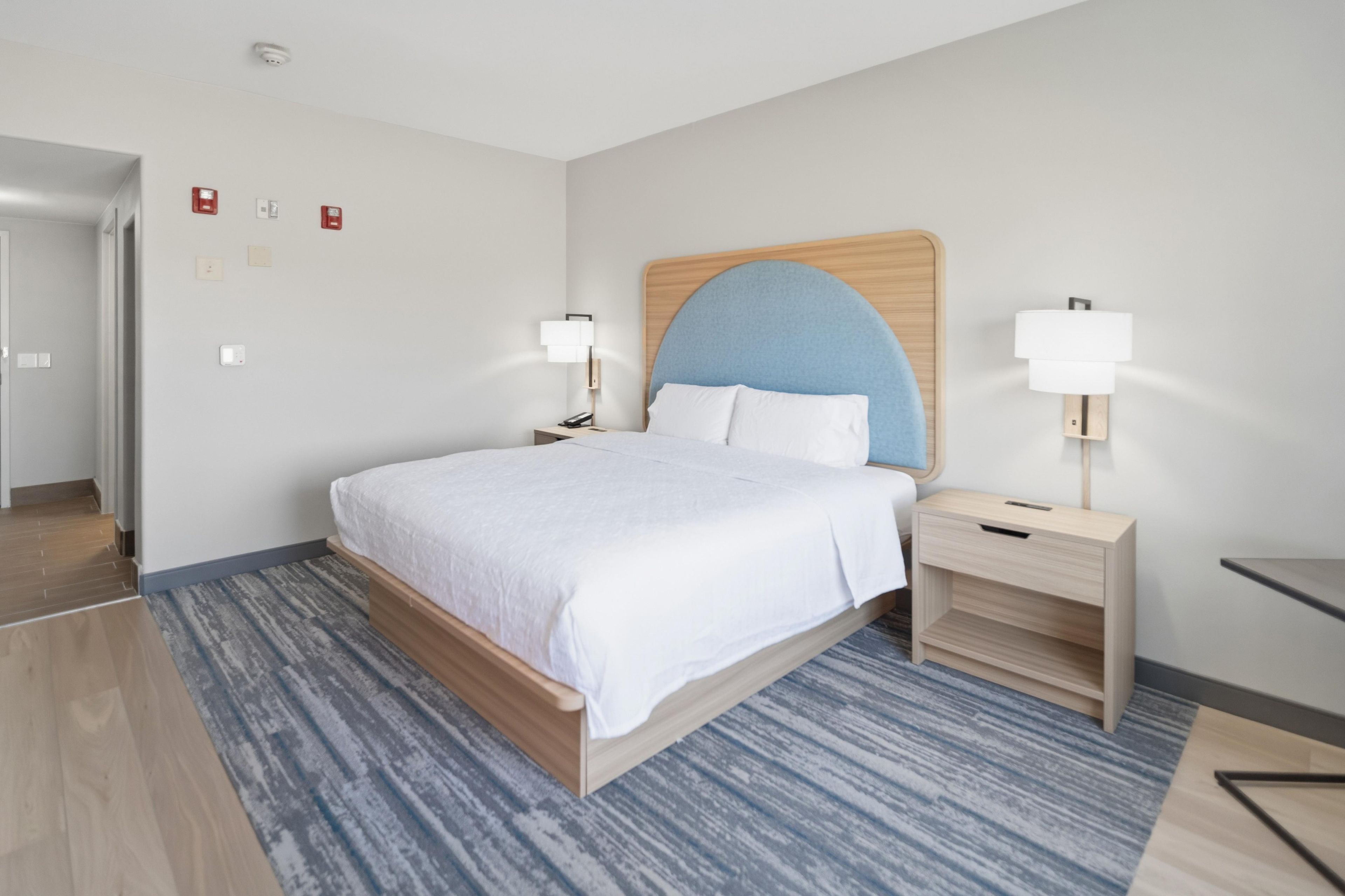 A hotel room with a bed, bedside tables, a lamp, and a blue accent wall.