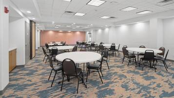 A conference room with multiple tables and chairs, carpeted flooring, and a white ceiling with recessed lighting.