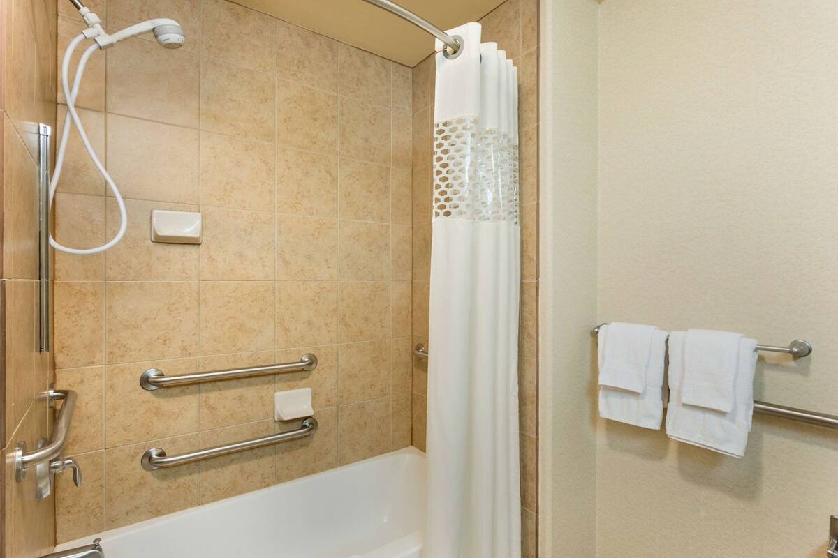 A bathroom with a bathtub, shower, grab bars, and a towel rack.