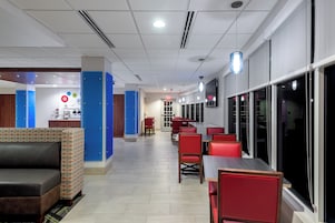 A modern indoor space with a long corridor, seating areas with red chairs, and a wall-mounted TV.