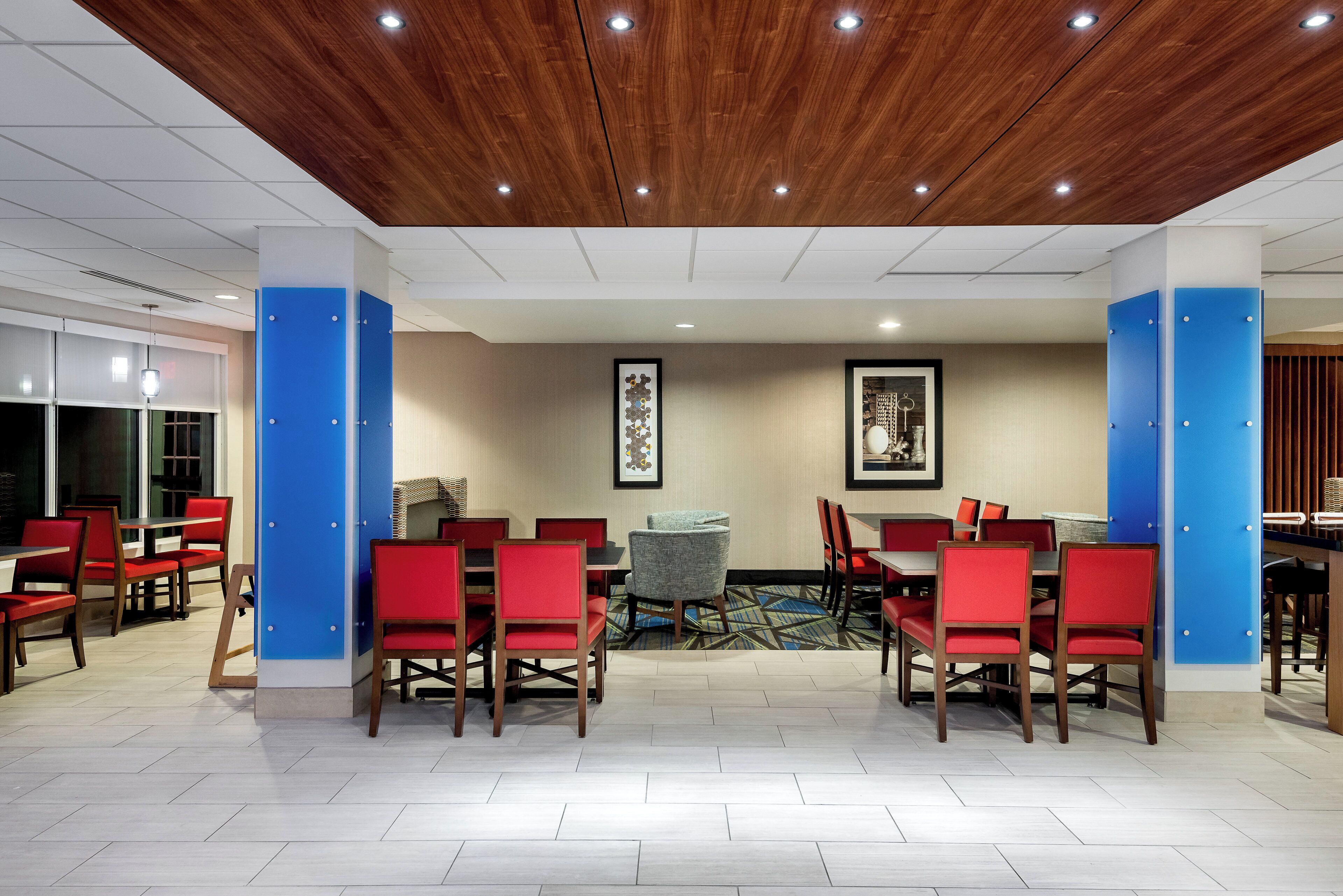 A hotel lobby with a wooden ceiling, blue pillars, red chairs, and a tiled floor.