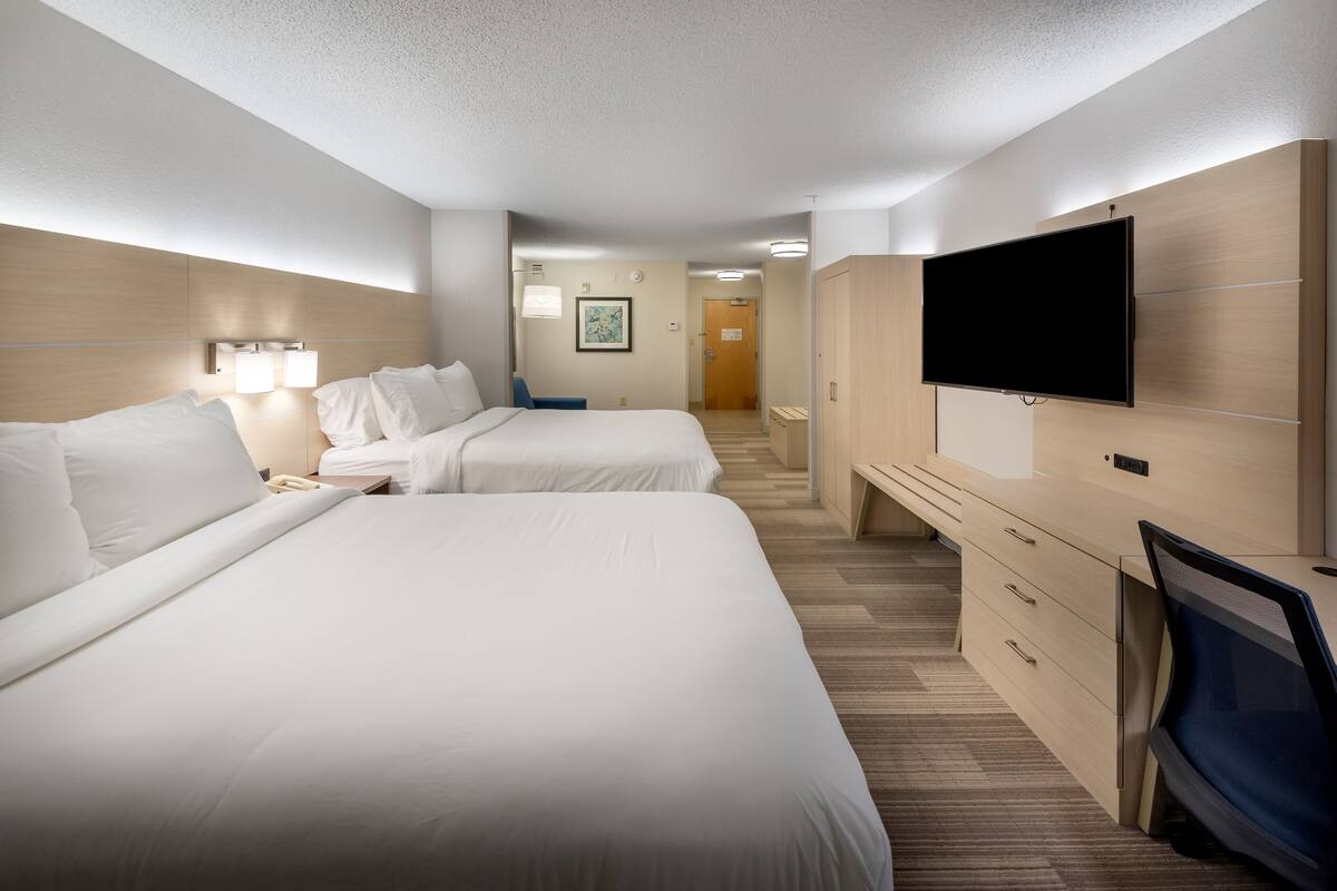 A hotel room with two beds, a desk, a TV, and a bathroom visible in the background.