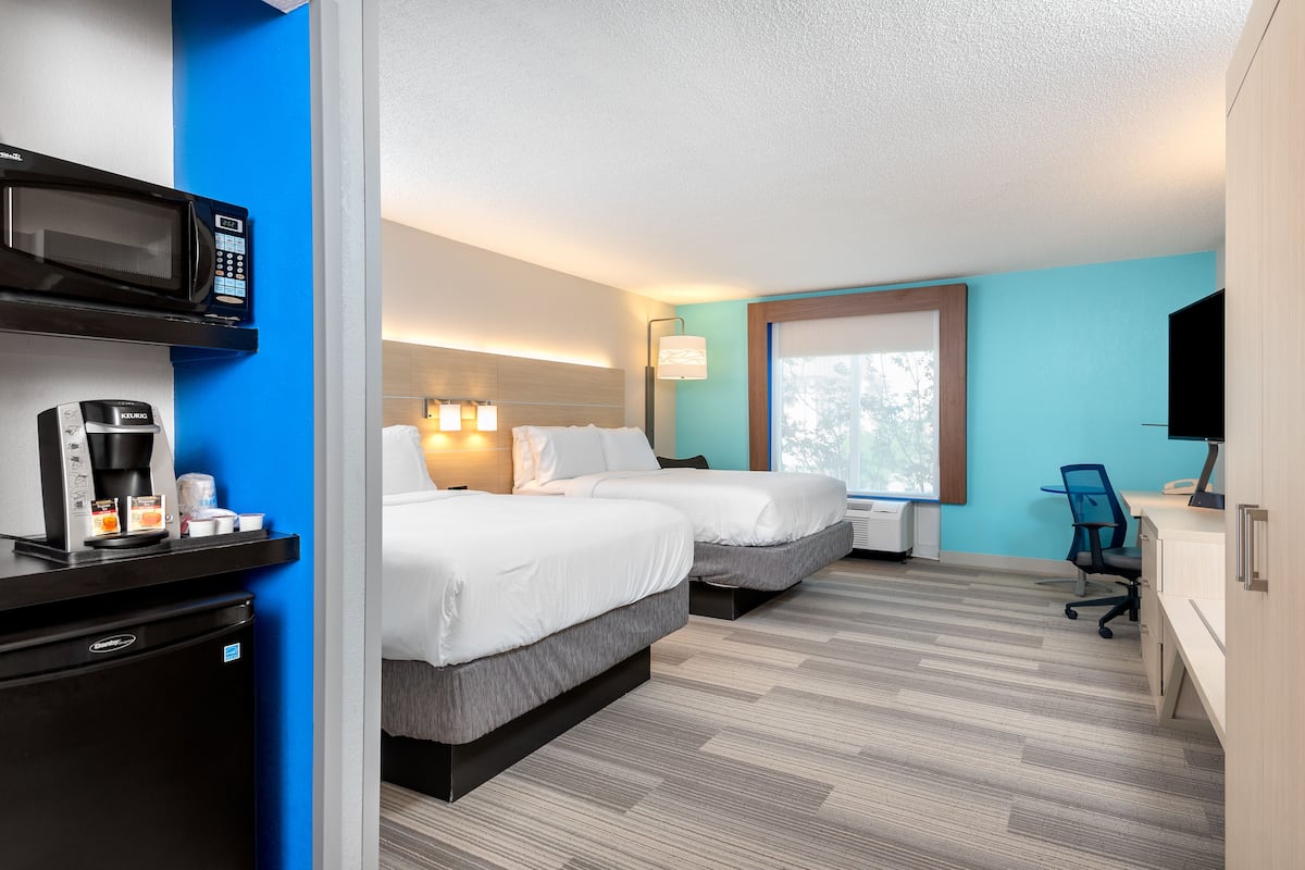 A hotel room with two beds, a microwave, a coffee maker, a desk, and a TV.
