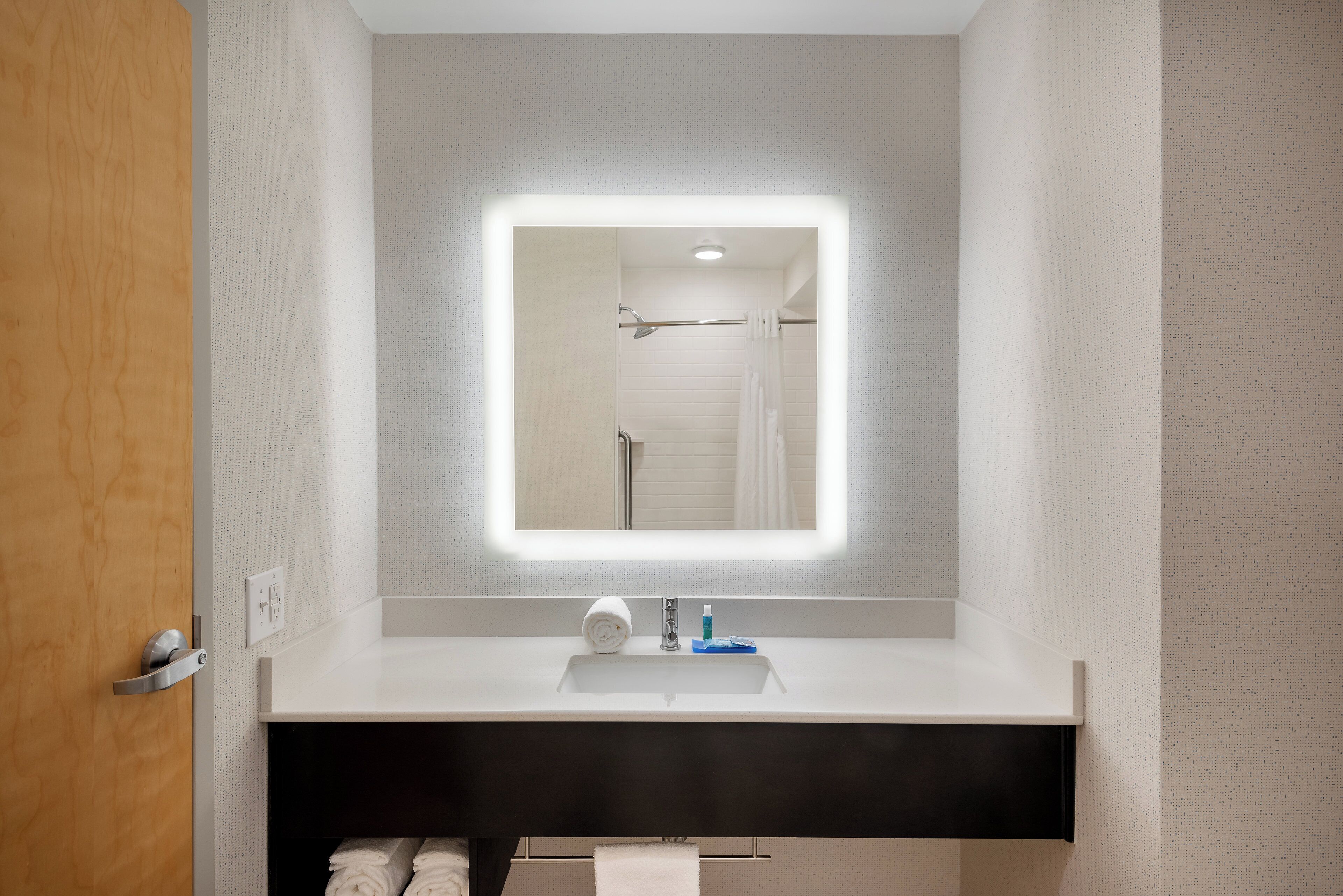 Un baño con un lavabo blanco, un espejo con luz y un perchero para toallas.