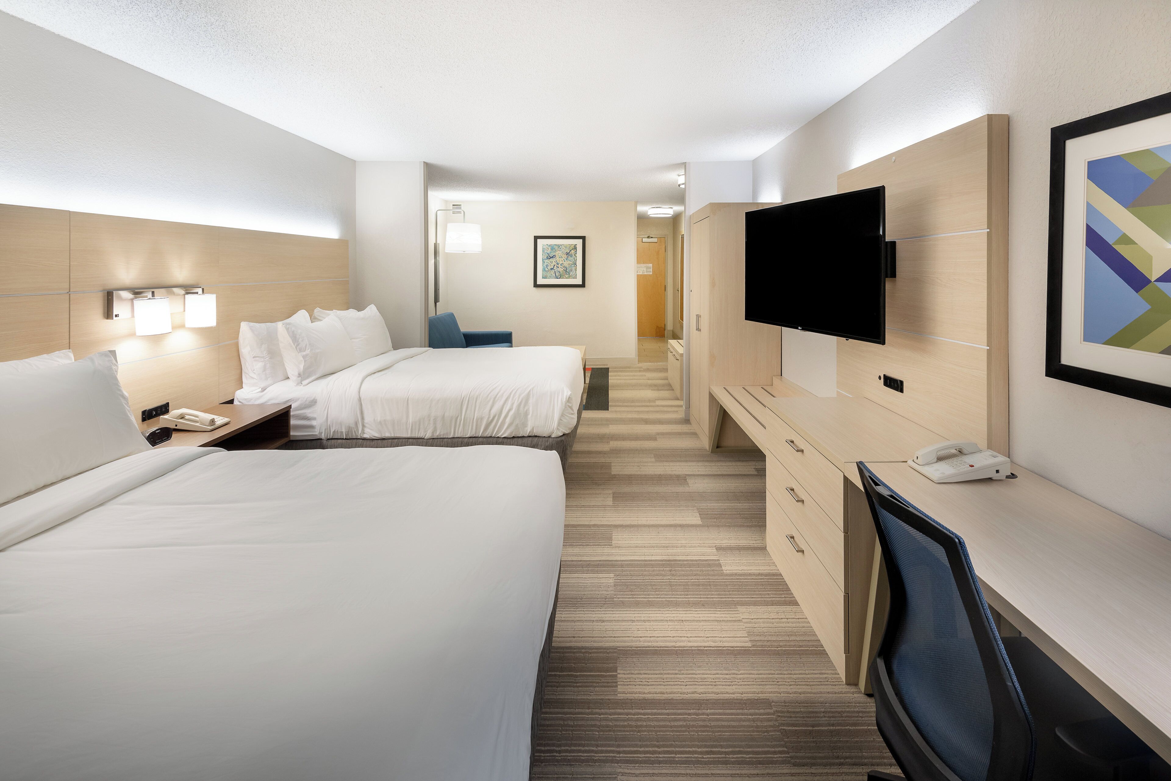 Une chambre d’hôtel avec deux lits, un bureau, une chaise, un téléviseur à écran plat et un téléphone.