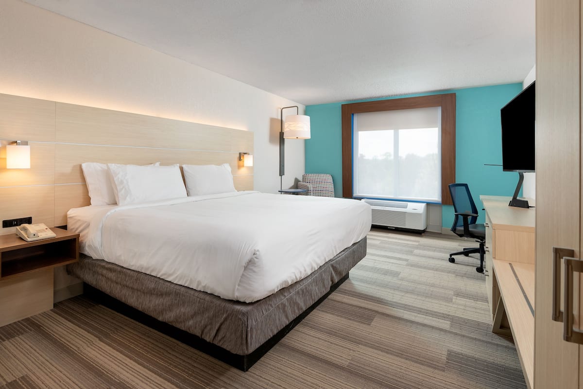 A modern hotel room with a large bed, bedside table with a phone, a desk with a chair, and a TV.