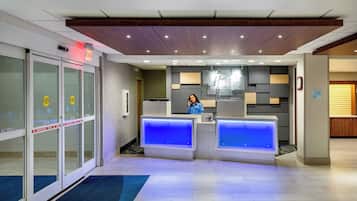 A hotel reception desk with a glass door entrance, a blue carpet, and a sign indicating an emergency exit.
