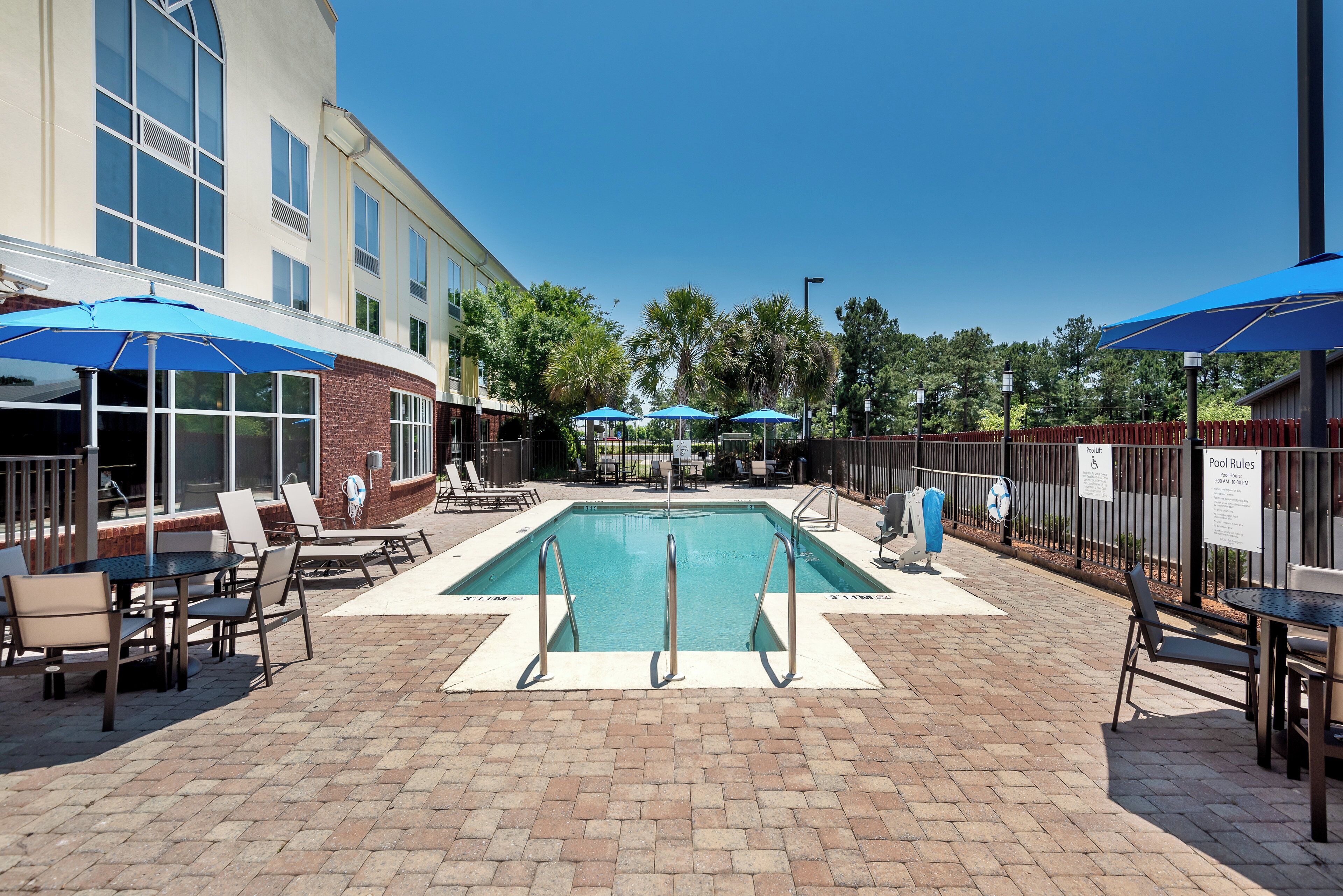 A pool area with a rectangular pool, lounge chairs, and umbrellas.