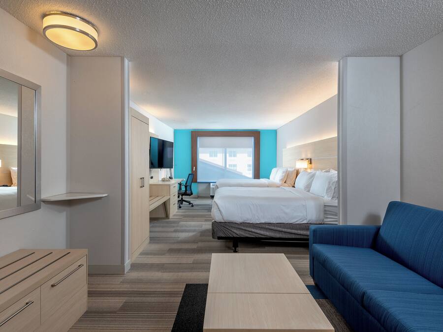 Quarto de hotel com uma cama, uma escrivaninha, uma televisão e um sofá azul.