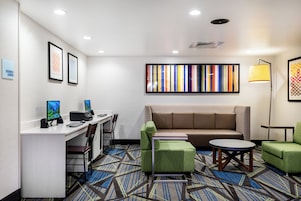 A hotel lobby with a reception desk, computers, seating area, and a colorful abstract painting.