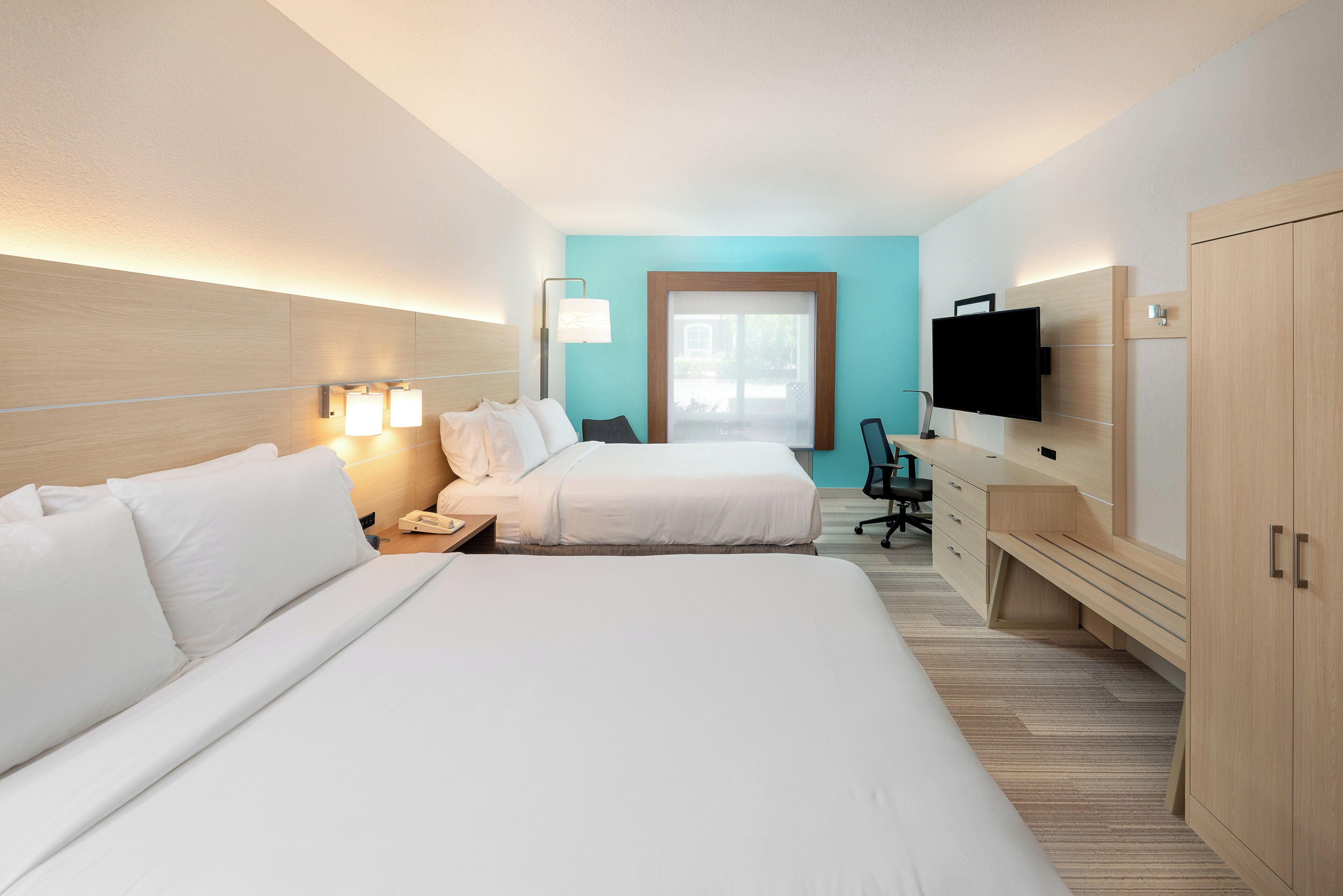 Habitación de hotel con dos camas, un escritorio, una televisión y una ventana con vistas.