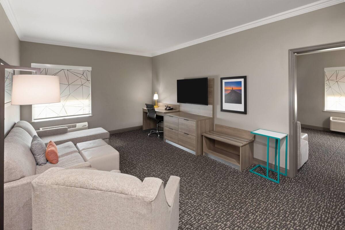 A hotel room with a sofa, a desk, a TV, and a window with a view.