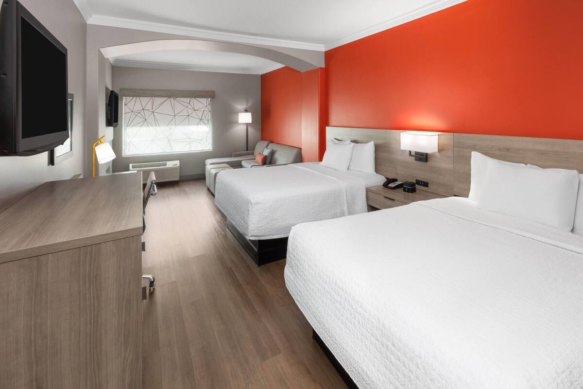 A hotel room with two beds, a desk, a TV, and a window with a geometric pattern.