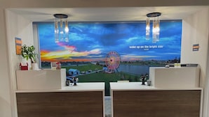 Zona de recepción de un hotel con un gran mural de un atardecer y una noria, dos mostradores de recepción y un letrero que dice 'La Quinta by Wyndham Moore, OK'.