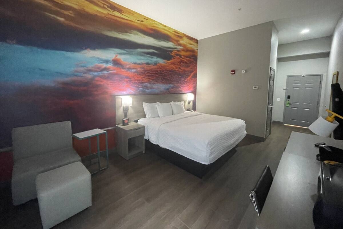 A hotel room with a large bed, a desk, a chair, a nightstand, and a wall mural.