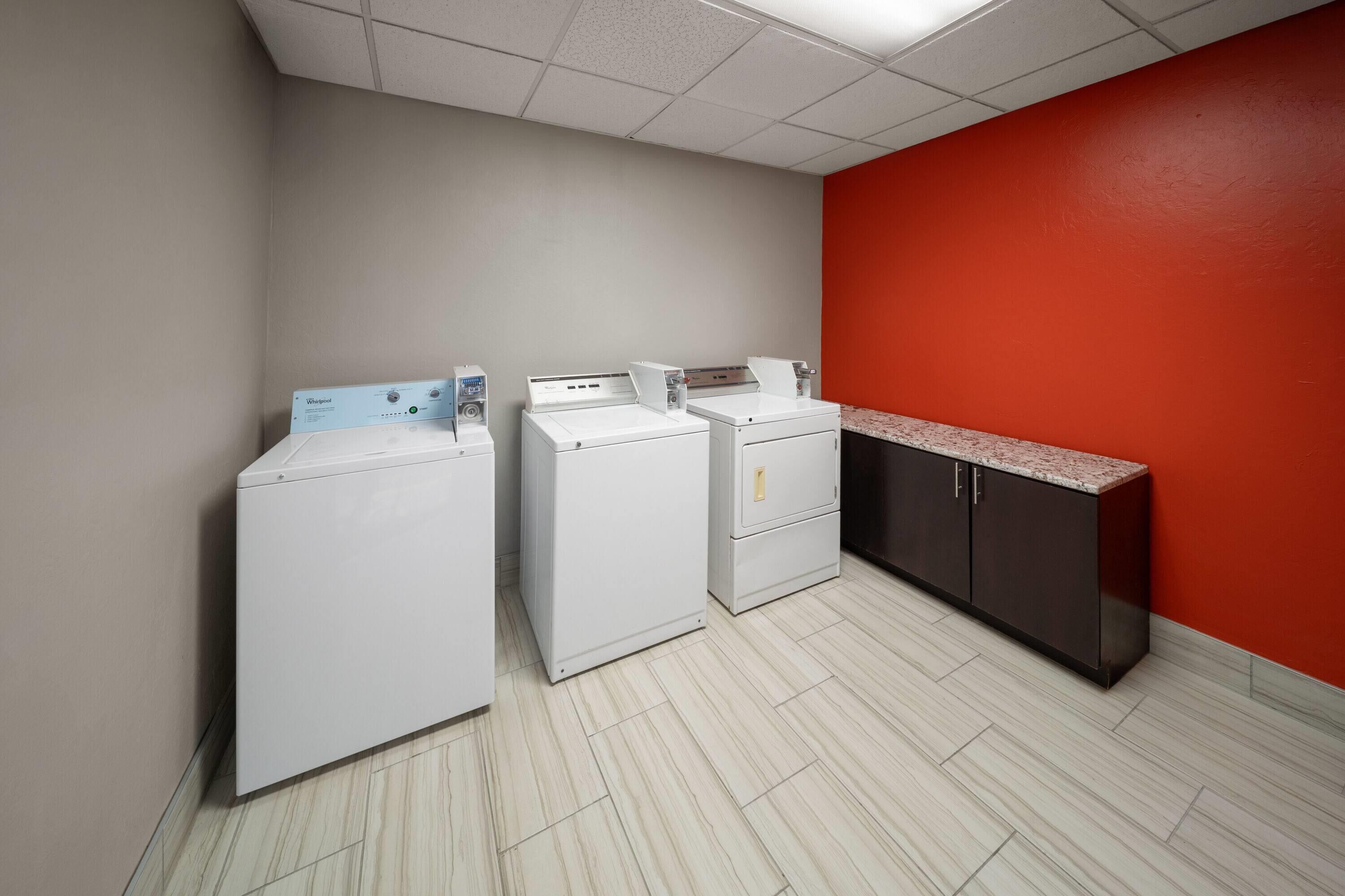 A laundry room with three white washers and dryers, a red wall, and a granite countertop.