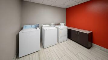 A laundry room with three white washers and dryers, a red wall, and a granite countertop.