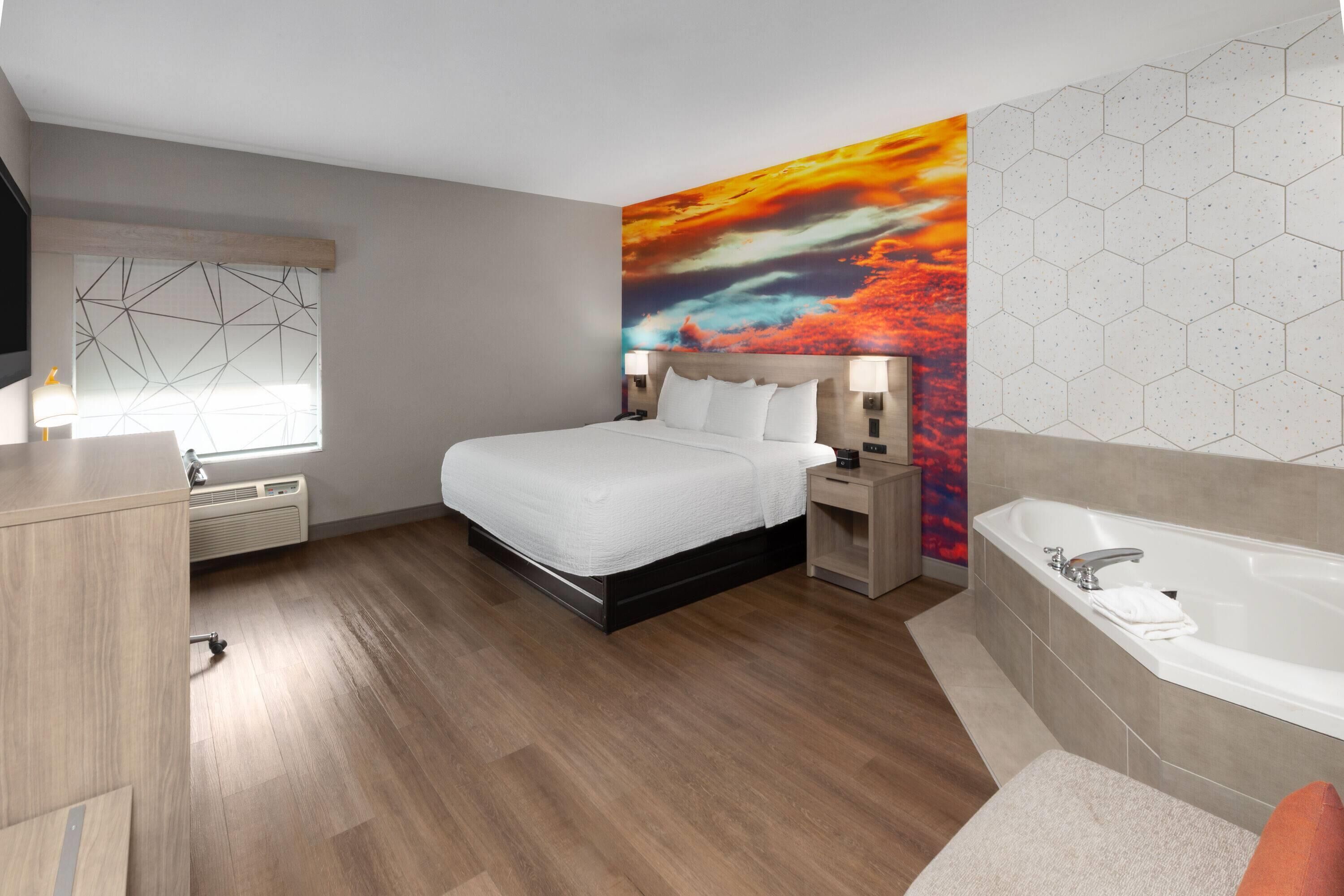 A modern hotel room with a large bed, a built-in desk, a vanity, and a separate bathroom with a bathtub.