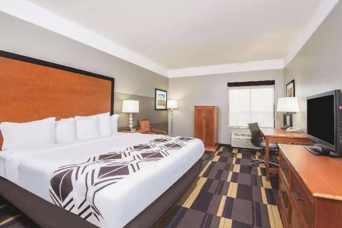 A hotel room with a large bed, a desk with a computer, a television, and a window.