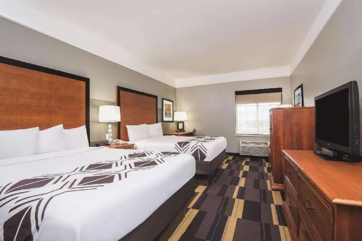 A hotel room with two beds, a television, a desk, and a window.
