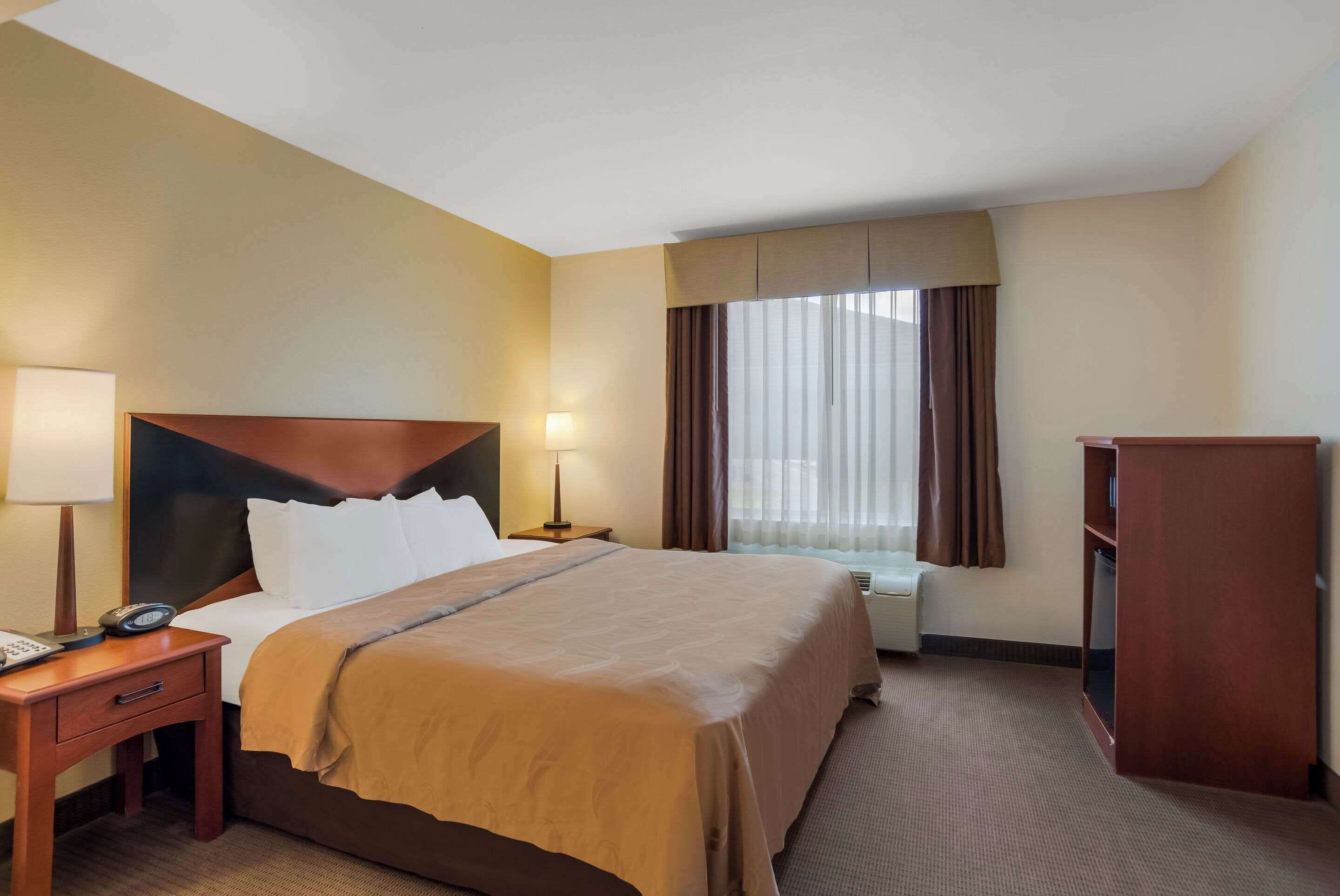 Ein Hotelzimmer mit einem großen Bett, einem Nachttisch mit Lampe, einem Kleiderschrank und einem Fenster mit Vorhängen.