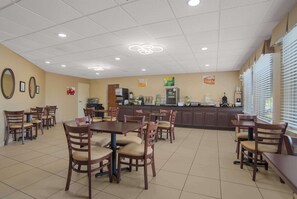 A spacious dining area with multiple tables and chairs, a kitchen area with appliances, and a counter for service.